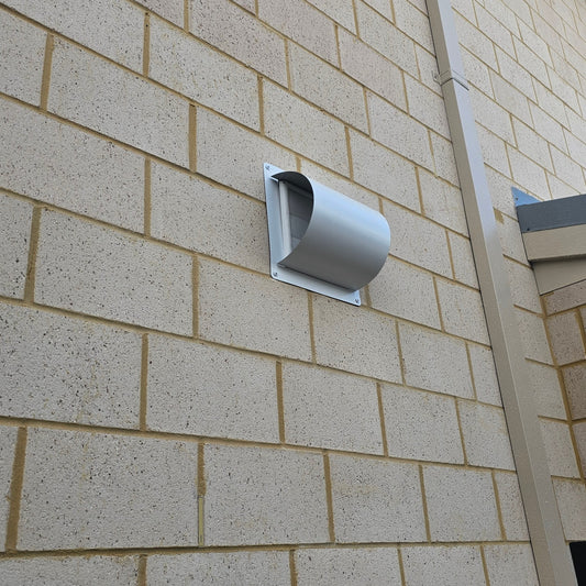 A white, decorative wall vent installed on a brick wall.
